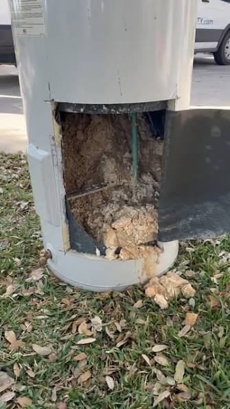 Water heater with its access panel opened showing packed sediment filling the tank